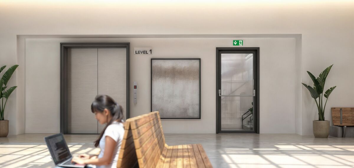 Woman with laptop sitting in bright lobby with escape door.