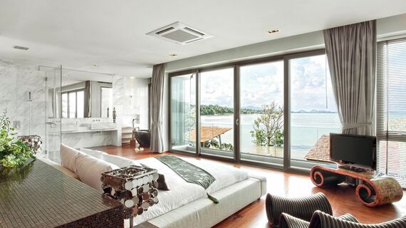 Interior view of a bedroom in the Eva Beach Resort in Thailand, with a Reynaers Aluminium lift-and-slide solution opening up to the beach and ocean.